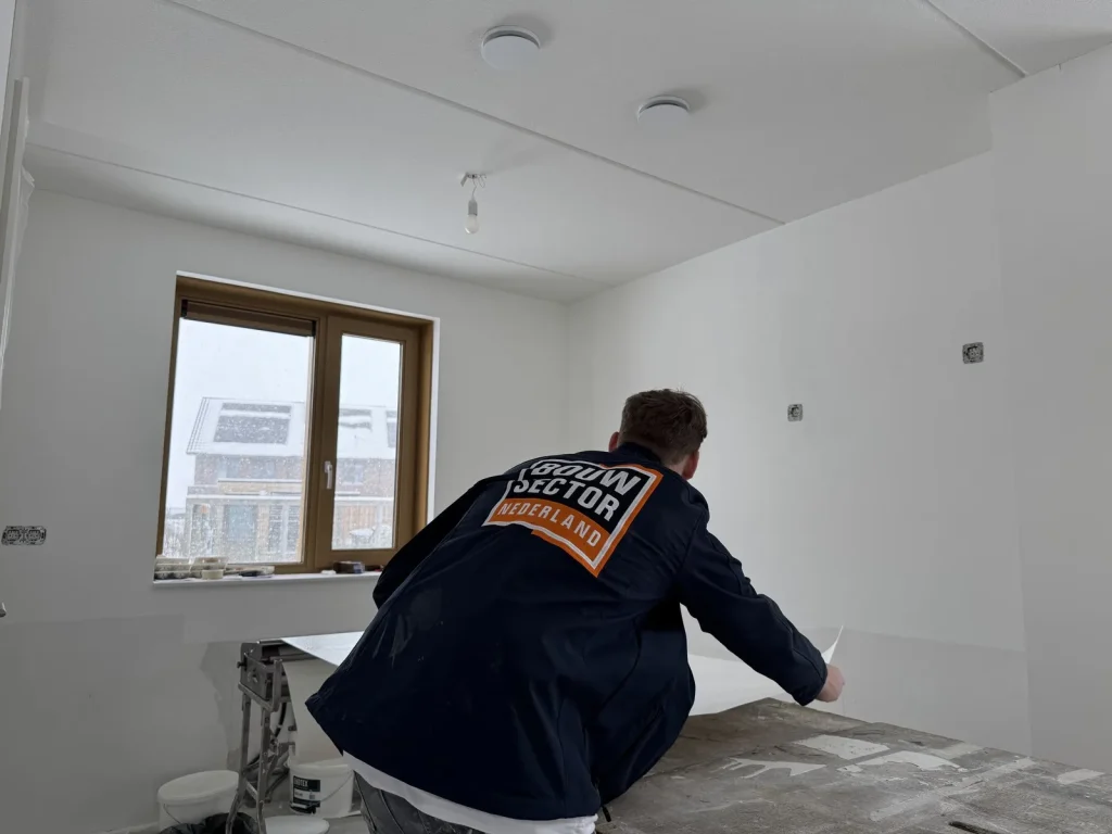 Behanger van Bouwsector Nederland rolt een baan renovlies uit over de plaktafel in een kale nieuwbouwkamer