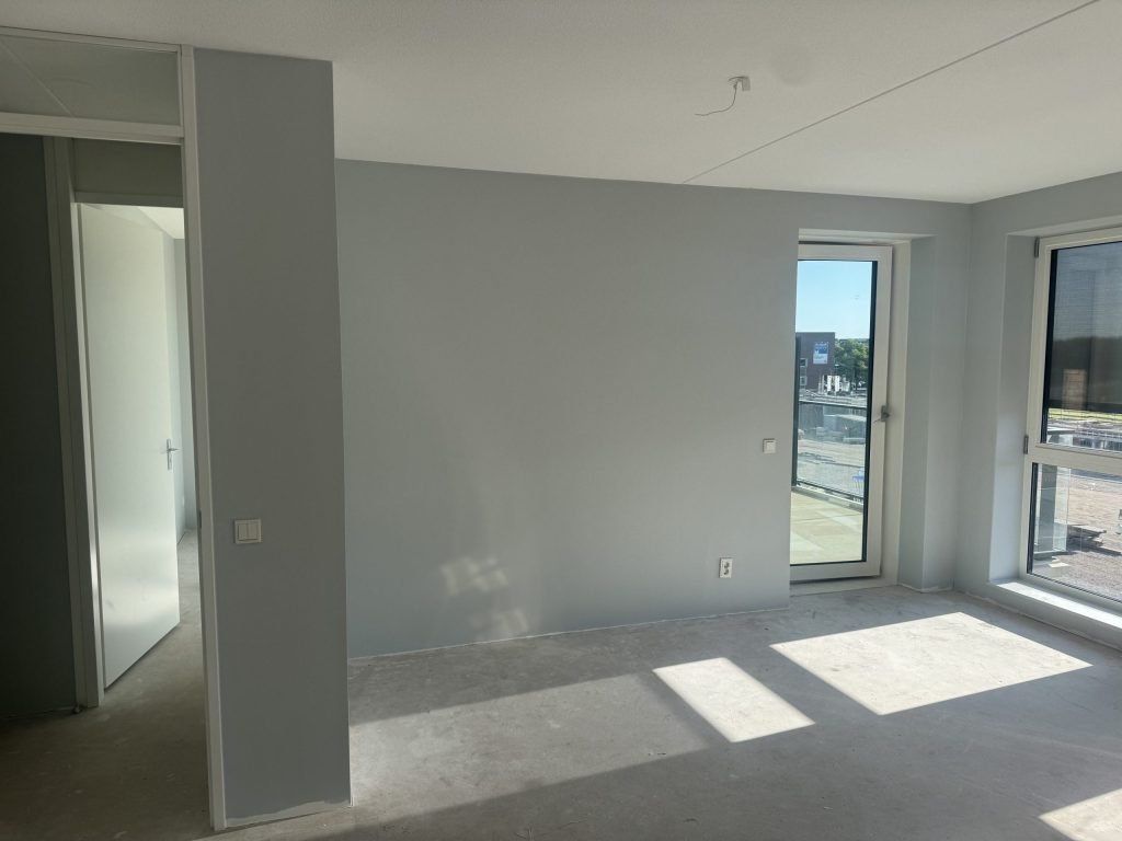 Lege nieuwbouwkamer met kale wanden, een betonvloer en een deur naar het balkon