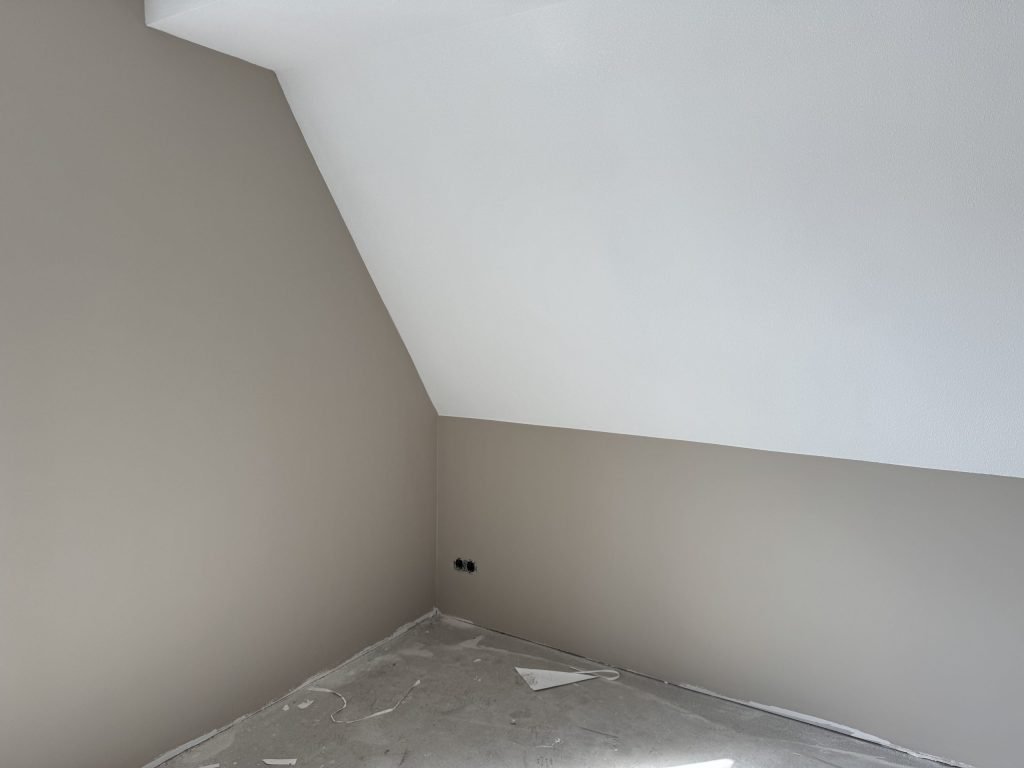 Zolderkamer in een nieuwbouwhuis met een schuine wand in wit en rechte wanden in een lichte taupe tint