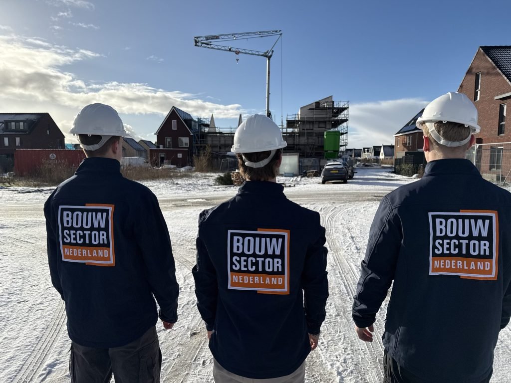 Drie vakmensen van Bouwsector Nederland met witte helm kijken naar een rij nieuwbouwwoningen in aanbouw